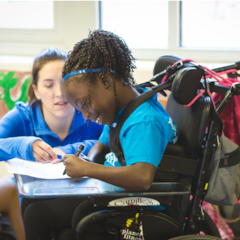 Smiling Girls on the Run participant in wheelchair writing as kneeling coach helps